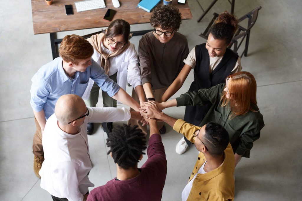 photo-of-people-holding-each-other-s-hands-3184436 Top view of diverse group of people collaborating in office setting.